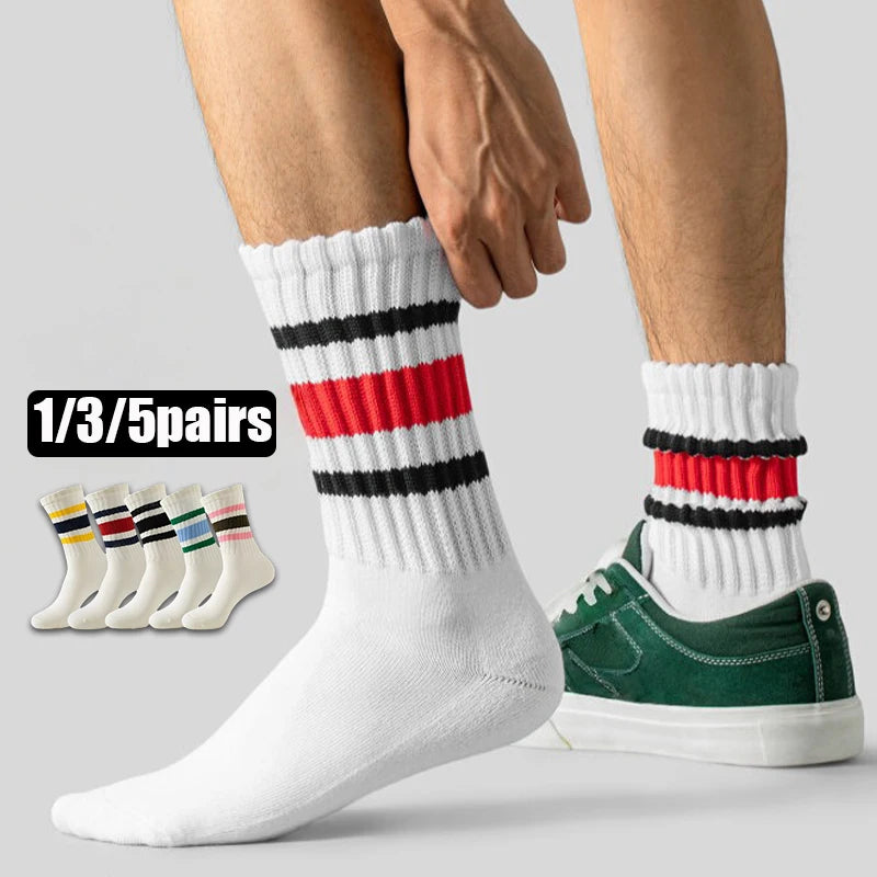 A pair of white crew socks with black and red horizontal stripes is shown on a foot, next to a hand.