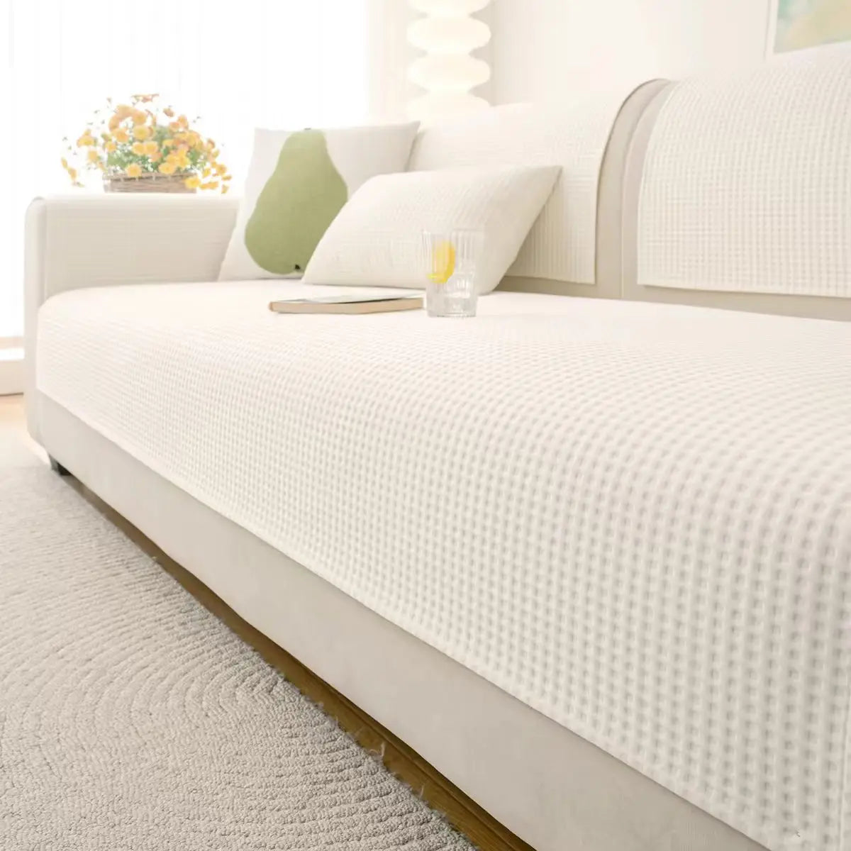 A white sofa slipcover with a textured fabric and light green accent pillows on a light rug.