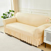 A beige dustproof stretch sofa slipcover displayed on a light wood floor with white trim and a window in the background.