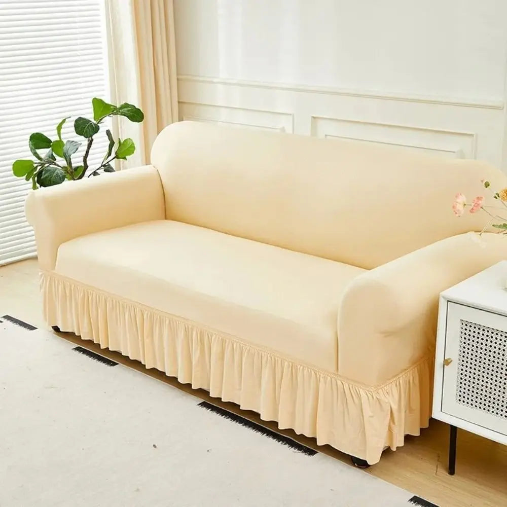A beige dustproof stretch sofa slipcover displayed on a light wood floor with white trim and a window in the background.