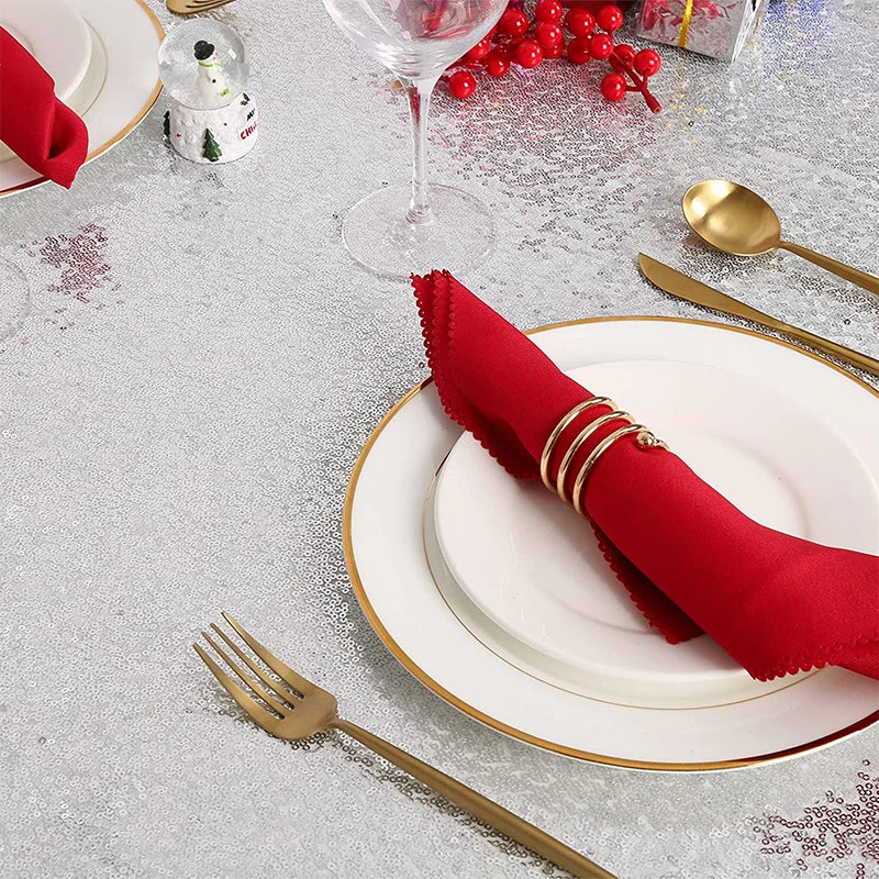A festive table setting featuring a red napkin, gold cutlery, and white plates on a silver glitter tablecloth.