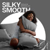 A woman with curly hair is relaxing on a bed, holding a satin pillowcase, with text promoting silky smooth skin.