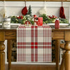 A red and white plaid linen checkered table runner displayed on a wooden table with festive greenery and holiday decor.