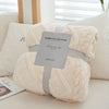 A fluffy cream colored throw blanket with a jacquard pattern is displayed on a white pillow.