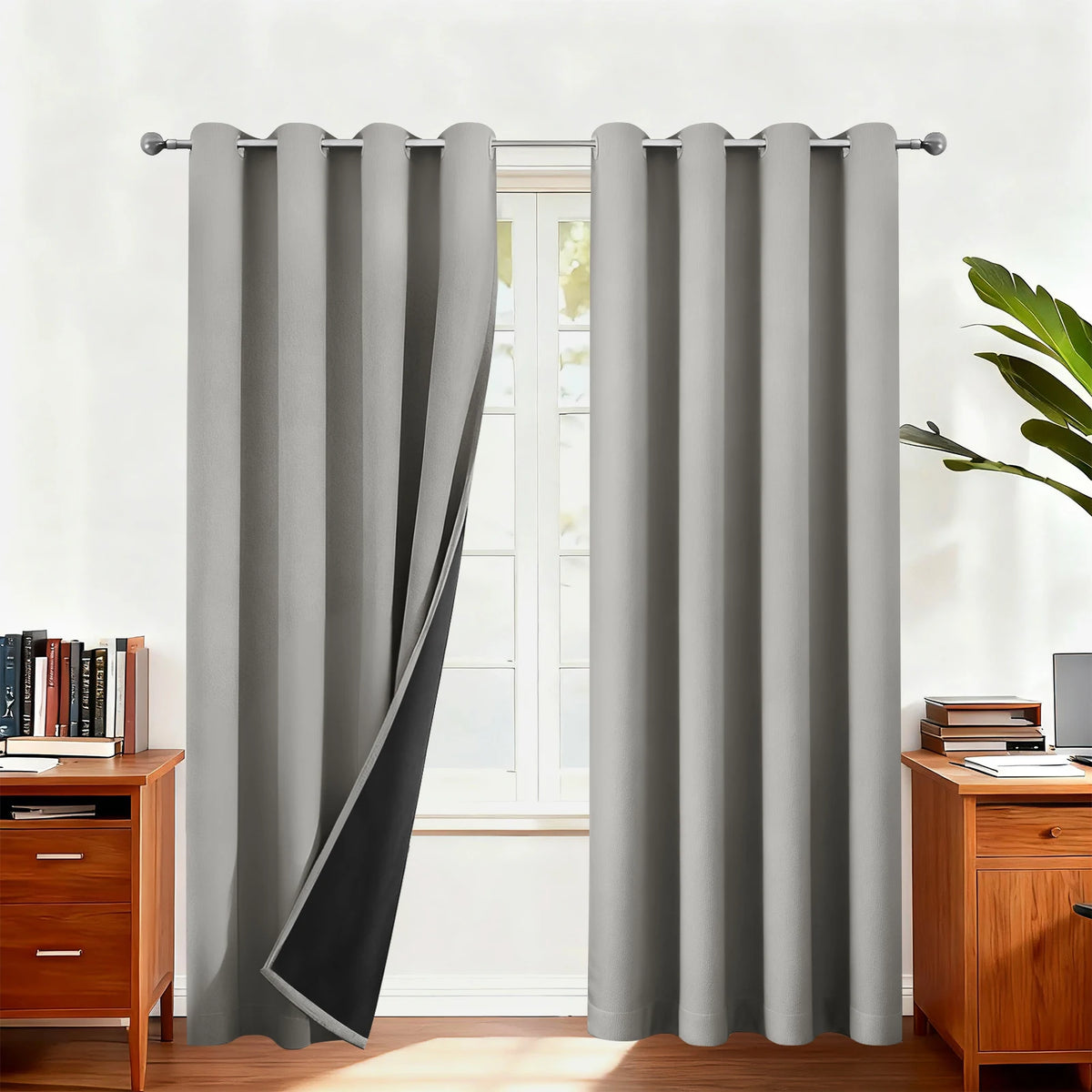 Gray blackout thermal window drapes hanging in a window frame with wooden furniture visible.