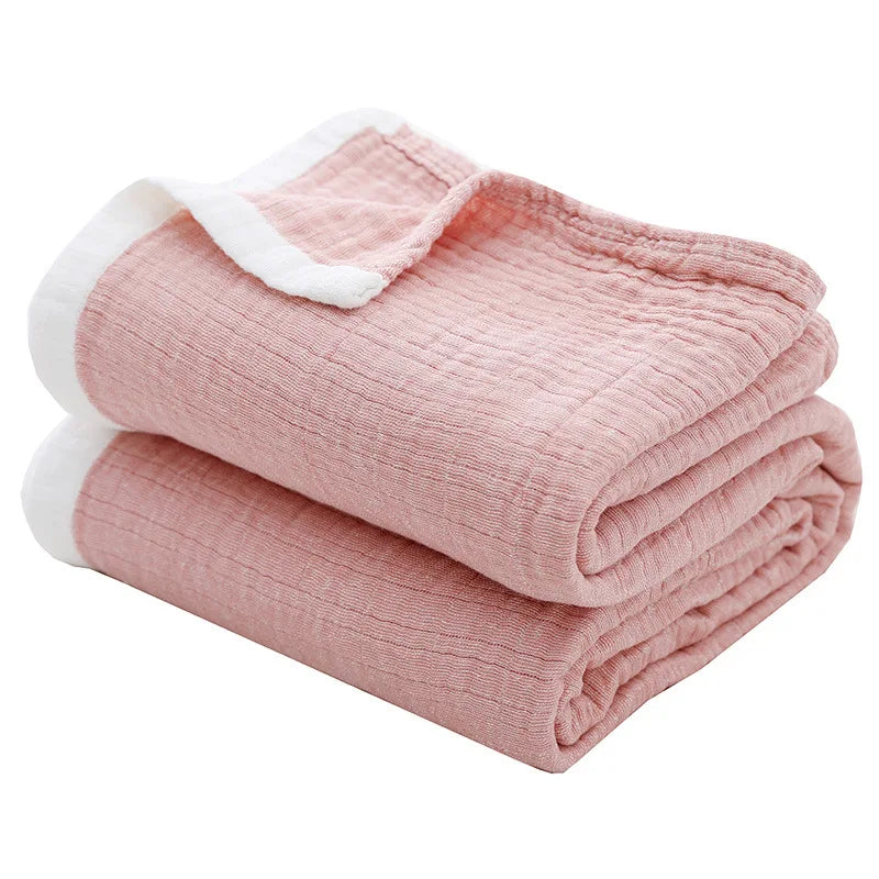 Pink muslin throw blanket folded and rolled with white trim