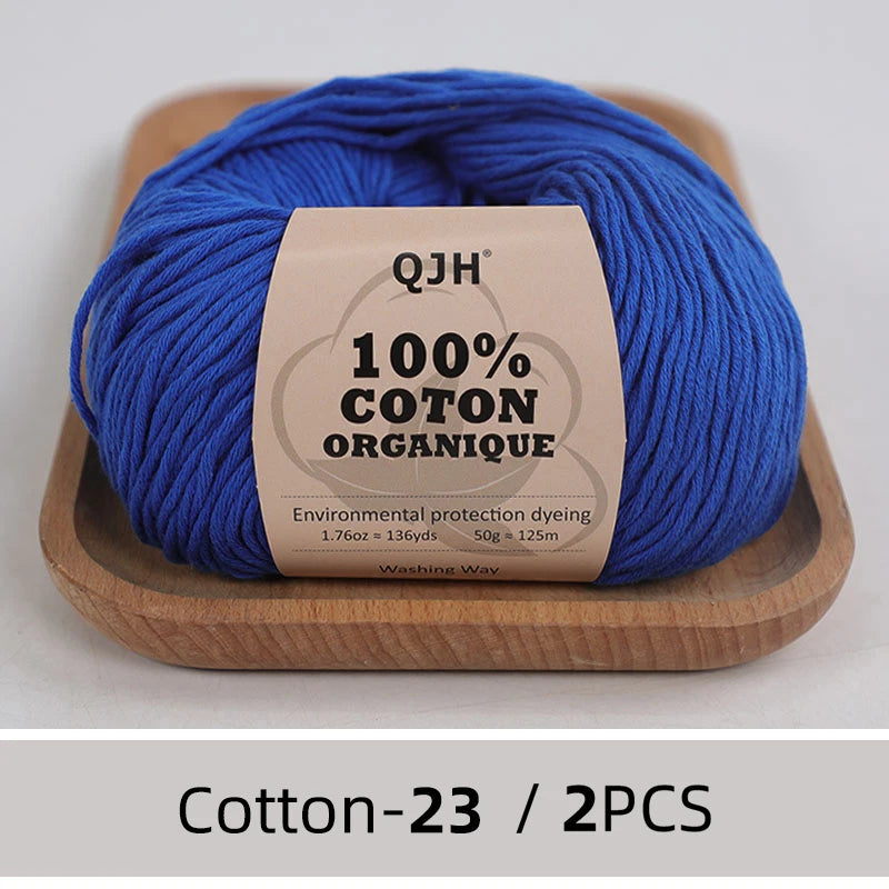 A ball of bright blue 100% organic cotton yarn labeled QJH for knitting and crochet on a wooden tray.