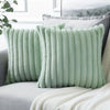 A light sage green stripe corduroy pillow cover resting on a gray sofa with a white knitted blanket.
