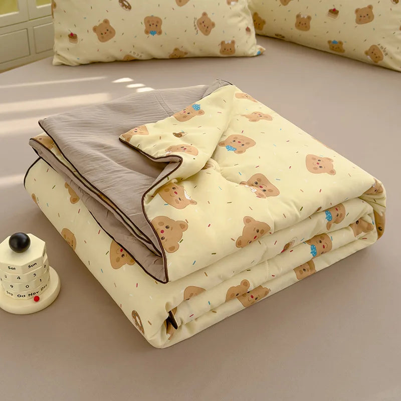 A folded light yellow quilt with a beige cover and a gray lining, featuring small brown animal patterns.