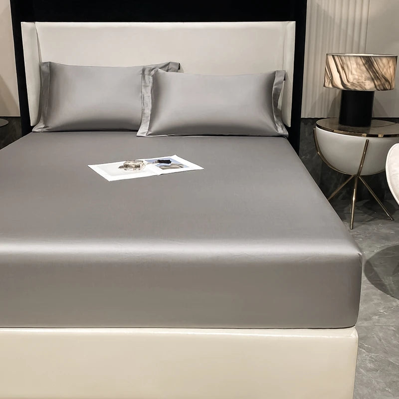 A luxury bed set featuring a fitted sheet, pillows, and a bedside lamp in neutral tones.