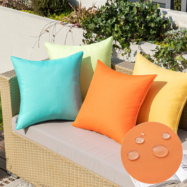 A collection of bright pastel outdoor pillow covers in shades of mint green, lime yellow, and orange resting on a woven outdo