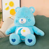A light blue Care Bears Rainbow Bear plush toy with white accents and blue heart details sitting on a green fabric.