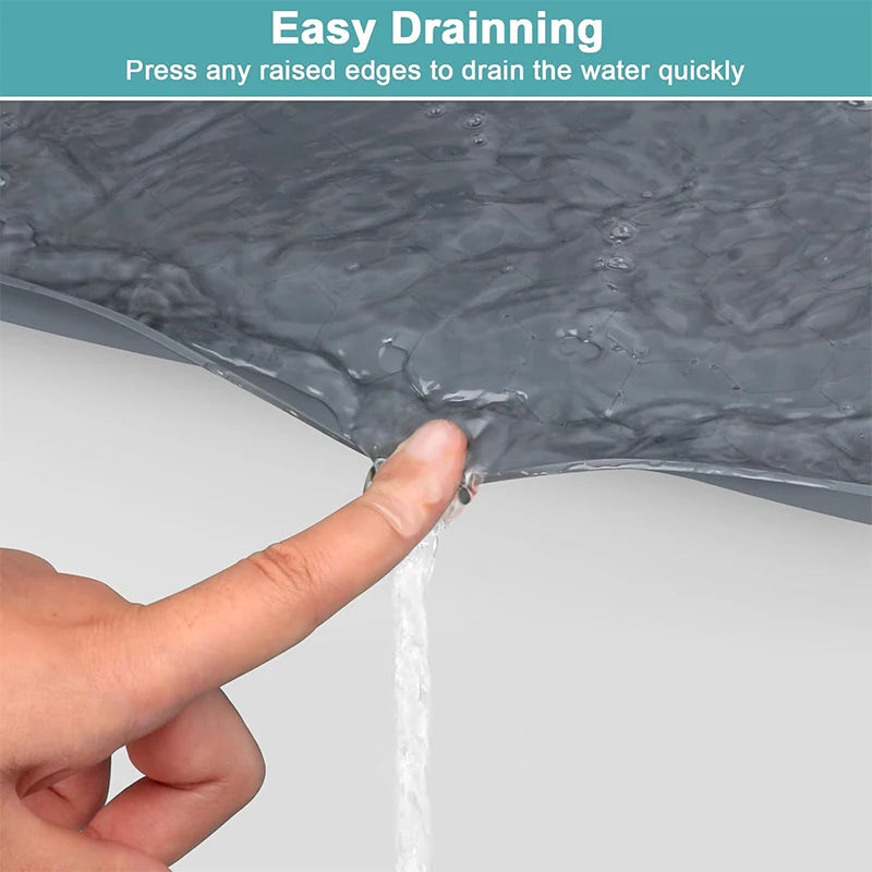 A hand is pressing a raised edge on a dark gray silicone drain mat to quickly drain water.