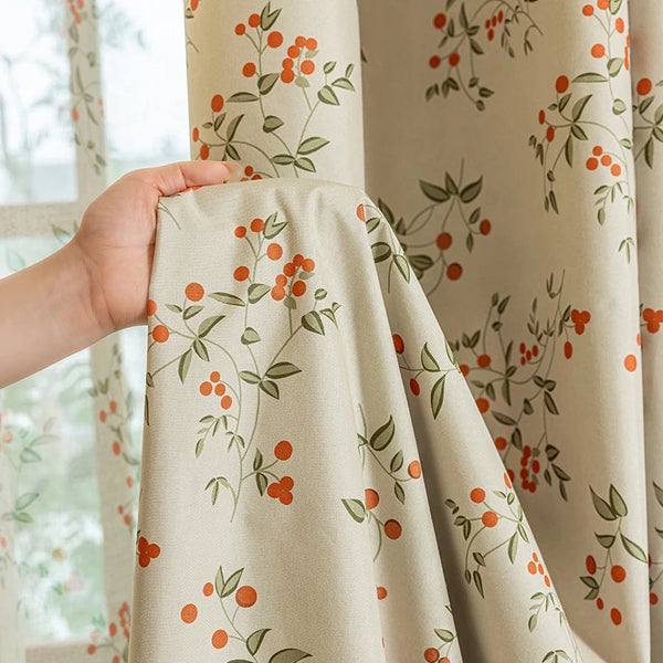 A close-up of beige curtains with a floral pattern featuring orange berries and green leaves.