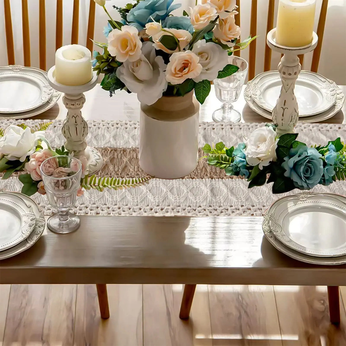 A rustic table setting featuring a linen runner, white plates, and floral arrangements with blue and peach roses.
