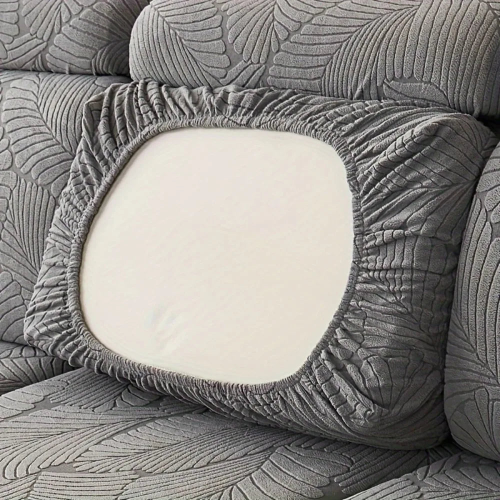 A close-up of a gray leaf pattern sofa slipcover featuring a square white cushion.
