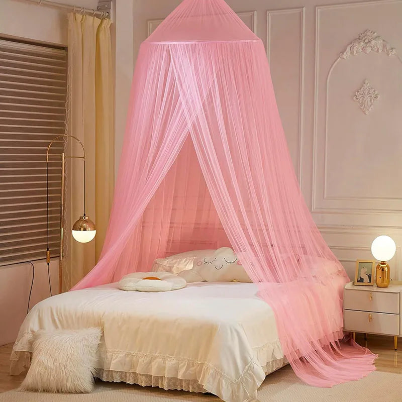 Pink sheer dome mosquito net draped over a bed with white bedding and fluffy accents.