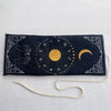 A dark blue pouch with a gold mystical design featuring symbols and a crescent moon, tied with a white cord.