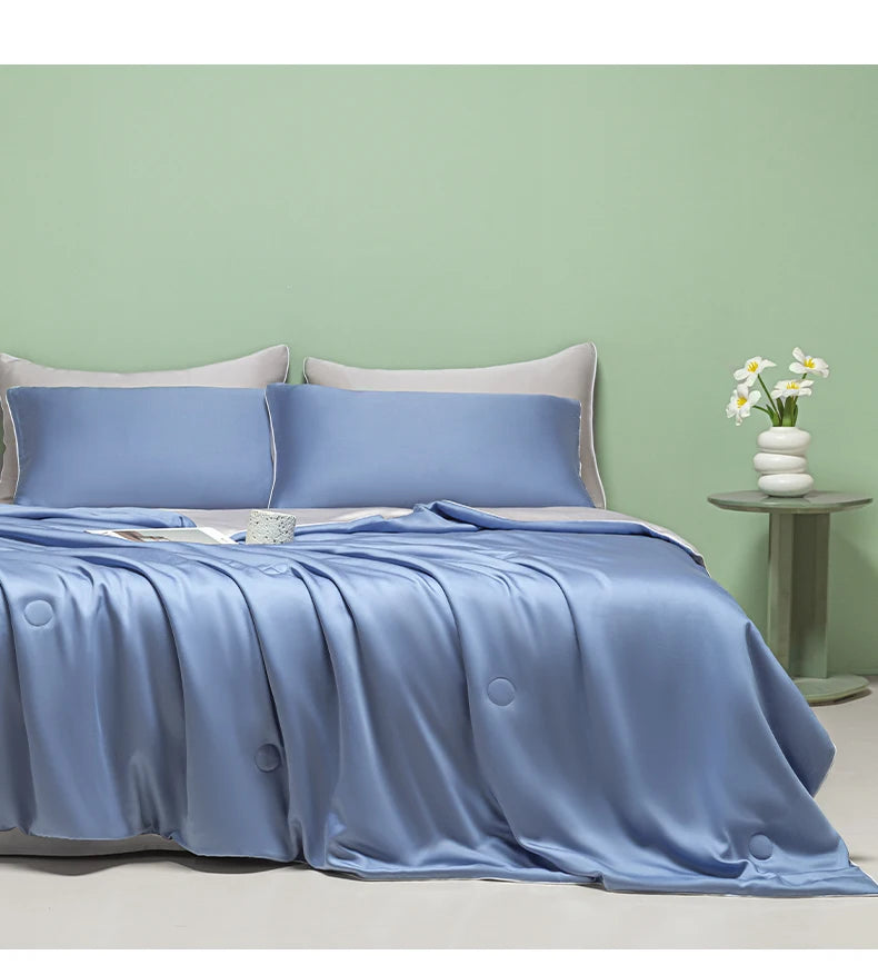 A light blue ice silk quilt draped on a bed against a pale green wall.