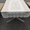 A rectangular dining table covered with a white cloth featuring gold and gray floral embroidery.