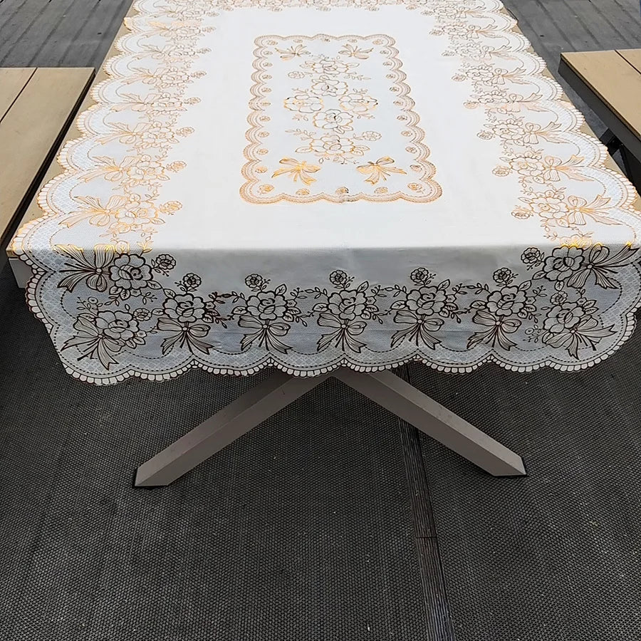 A rectangular dining table covered with a white cloth featuring gold and gray floral embroidery.