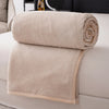 A stack of beige flannel throw blankets rolled and folded on a white surface.