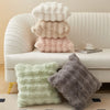 A collection of fluffy plush cushion covers in cream, beige, and pink resting on a white sofa.