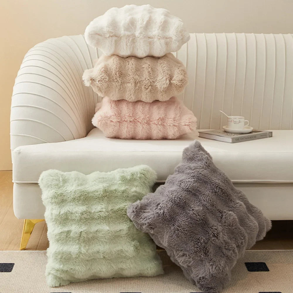 A collection of fluffy plush cushion covers in cream, beige, and pink resting on a white sofa.