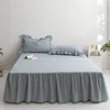 A light blue and white plaid cotton bed skirt cover draped over a bed in a bright room.