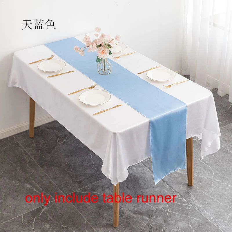 A white tablecloth set with a light blue satin table runner, white plates, and pink floral arrangement.