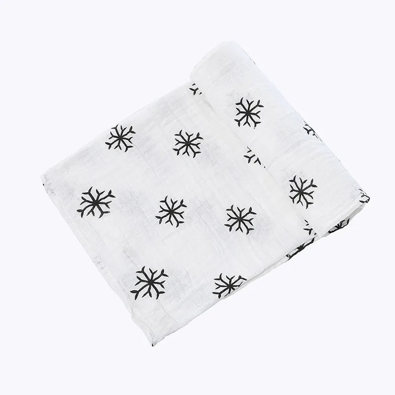 A white muslin swaddle blanket with a black snowflake pattern folded diagonally.