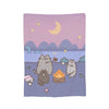 A soft purple blanket featuring a watercolor illustration of cats under a crescent moon and rolling hills.