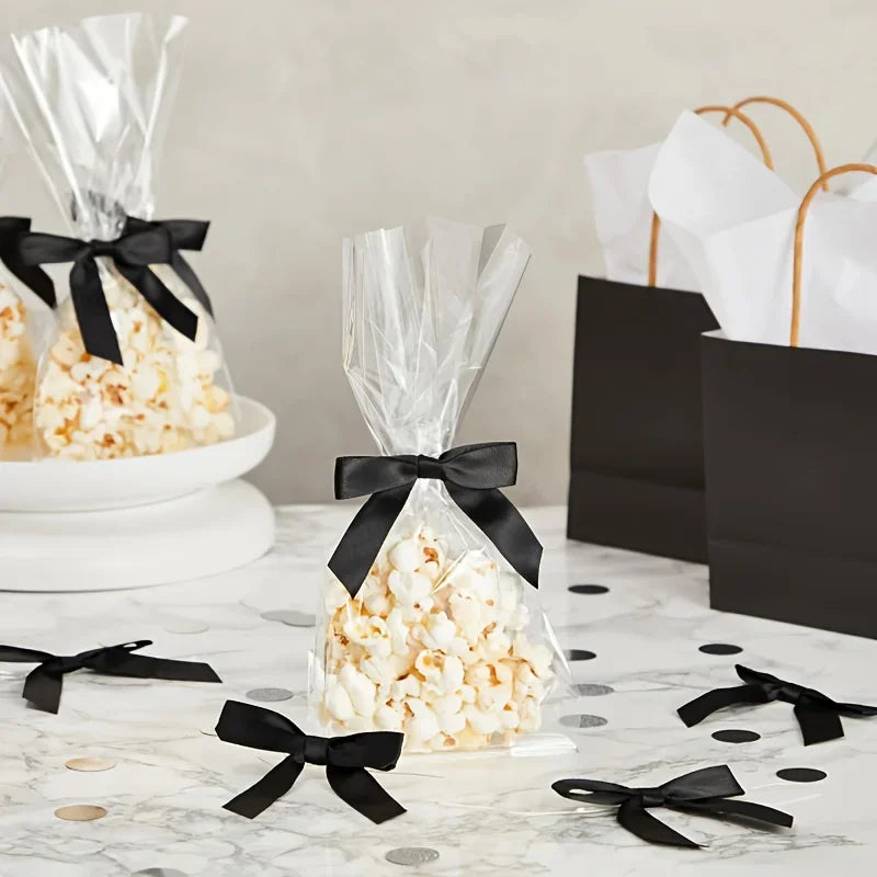 A display of white popcorn in clear bags tied with black satin ribbon bows on a marble surface.