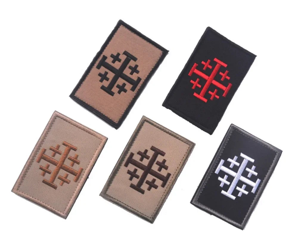 Four embroidered patches featuring a cross design in brown, black, red, and silver thread.