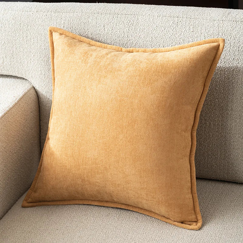 A square, mustard yellow chenille throw pillow resting on a light beige sofa.