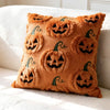 A textured, orange fuzzy throw pillow covered in repeating carved pumpkin designs.