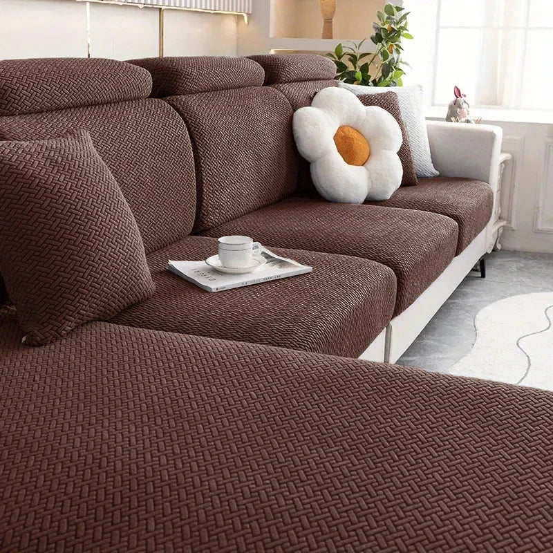 A brown textured sofa seat cushion cover with a white decorative pillow and a cup on the fabric.
