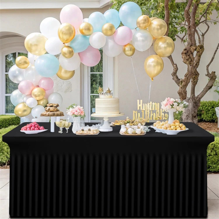 A display of pastel and gold balloons arranged on a black table, featuring a tiered cake and various treats.