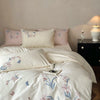 A white duvet cover set with embroidered pink and blue orchids and a lace trim on a bed.