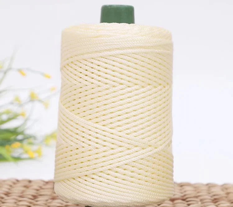 A spool of cream-colored crochet ice rope with a green cap resting on a woven mat.
