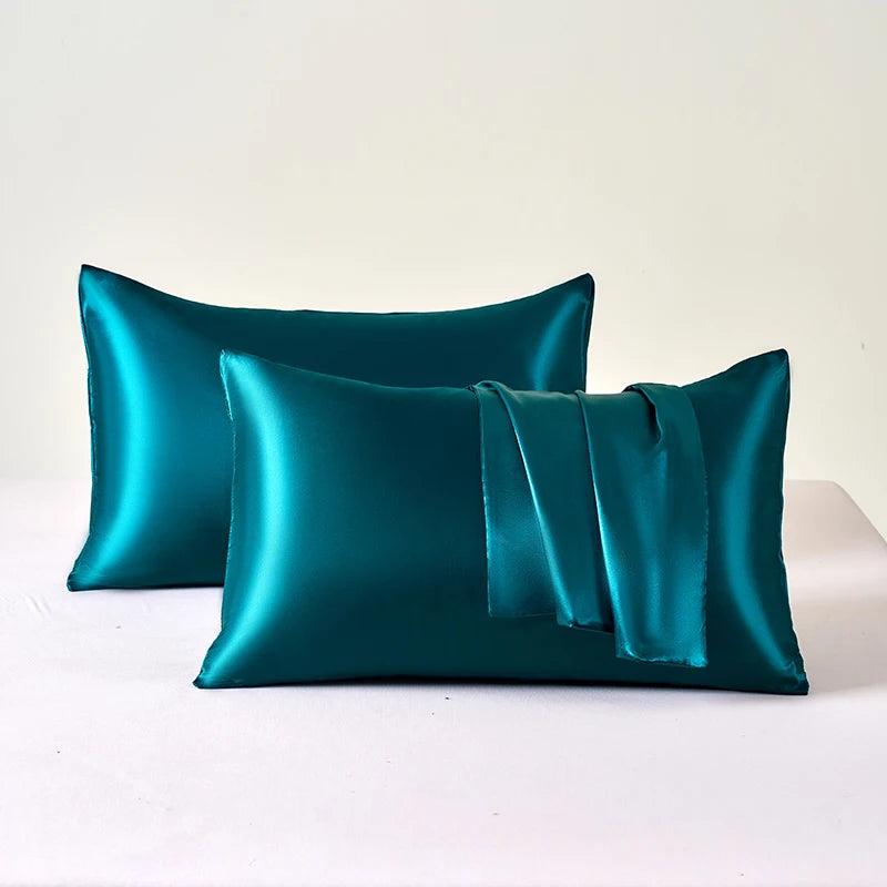 A set of two emerald green satin pillowcases, one folded with a sash, resting on a white surface.
