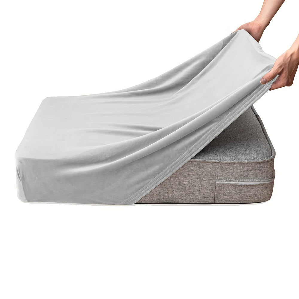 A hand is draping a light gray velvet stretchy sofa seat cover over a cushion.