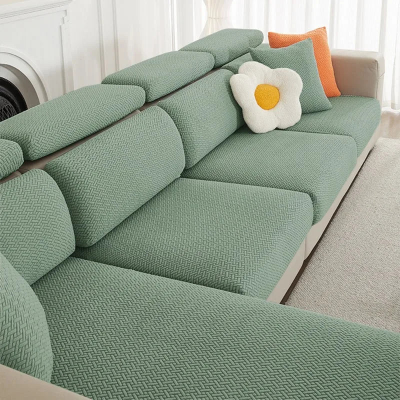 A light sage green jacquard elastic sofa cushion slipcover with a textured weave and an orange accent pillow.