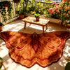 An irregular shaped plush floor rug in shades of orange and red is displayed on a wooden bench outdoors.