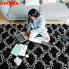 A person sits on a black geometric plush area rug in a living room, working on a laptop.
