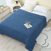 A navy blue pure cotton gauze throw blanket draped over a white bed with yellow patterned pillows.