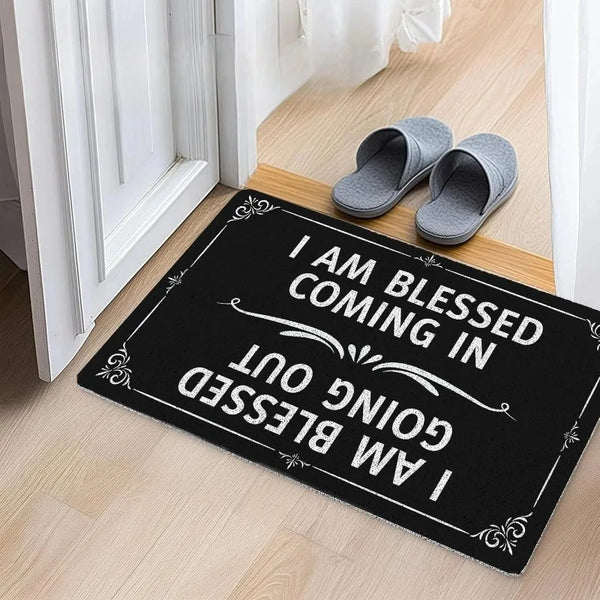 Black doormat with white text that reads I am blessed coming in I am blessed going out and features two slippers