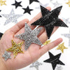 A hand holds several black and silver glitter rhinestone star iron-on patches for clothing.