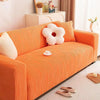 An orange stretchable sofa cover with white decorative pillows and a small cup on the surface.