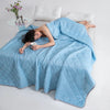 A woman is lying on a light blue quilted blanket in a bed, resting her head and holding a cup.